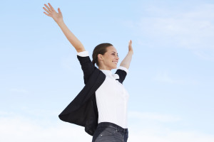 Young businesswoman with arms out against blue sky